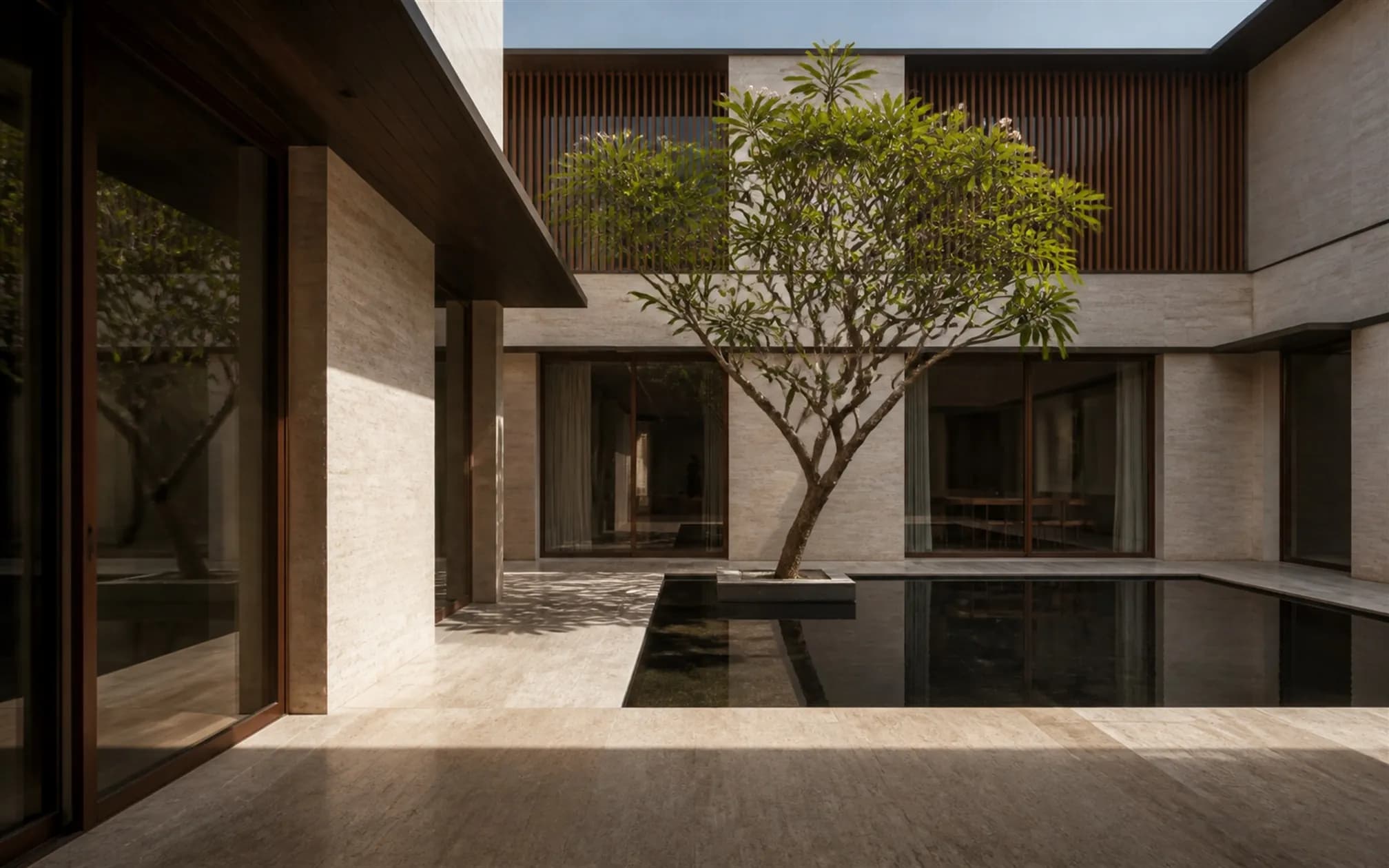 Private internal courtyard with a mirror-still reflecting pool and a mature frangipani, enclosed by travertine walls and teak screens
